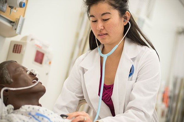 Student wearing scrubs practicing on a manikin