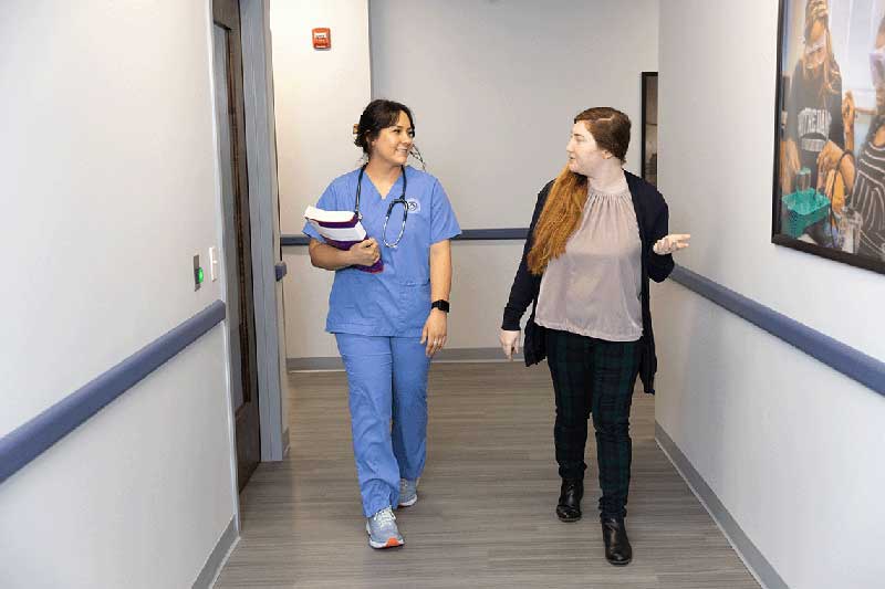 NDMU student in scrub walking hallway with woman
